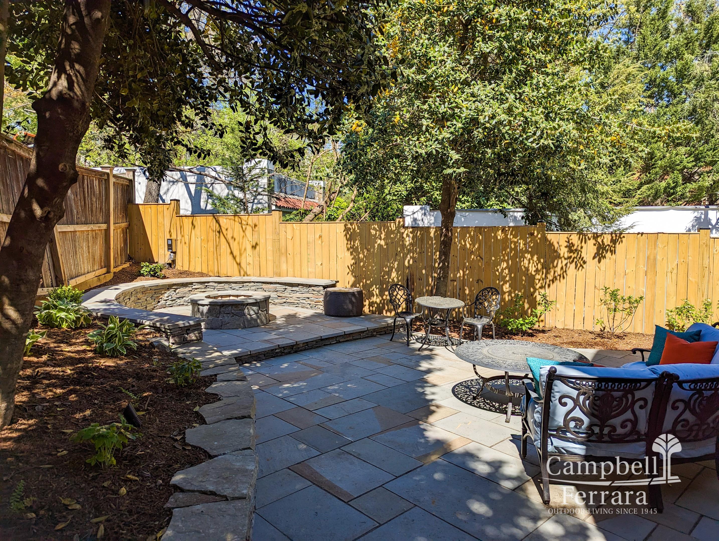 A stone fire pit with a seat wall installed around it on a flagstone patio